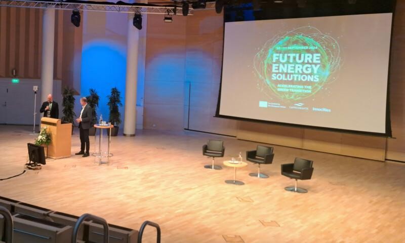 Lappeenranta Hall and Future Energy Solutions Conference logo slide on the wall. Two men on the stage.